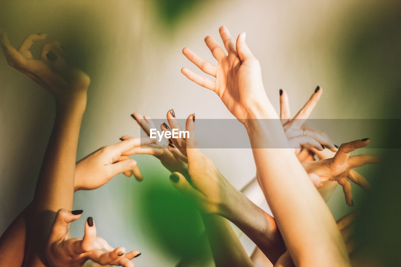 Cropped hands of female friends with arms raised against wall