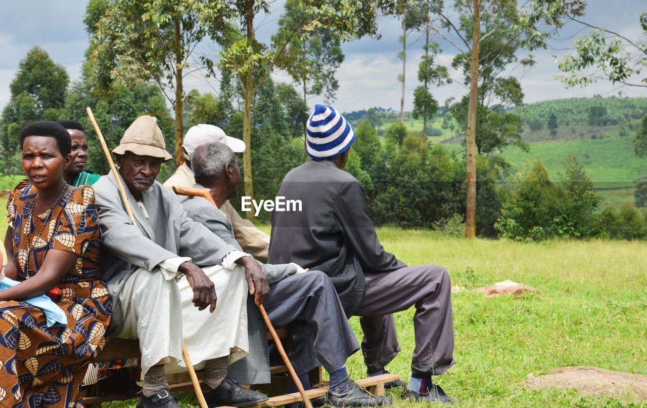 GROUP OF PEOPLE SITTING ON FIELD BY TREES