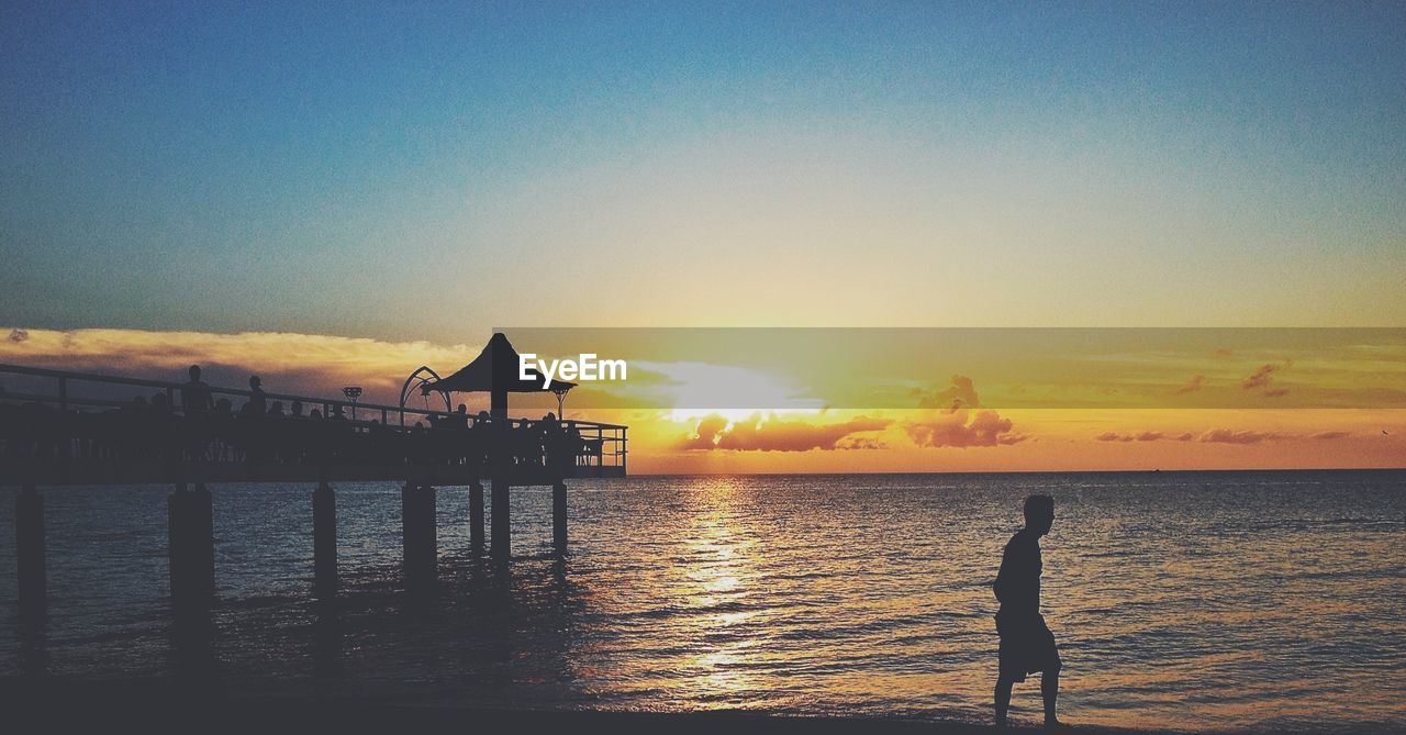 Silhouette man by pier at beach during sunset