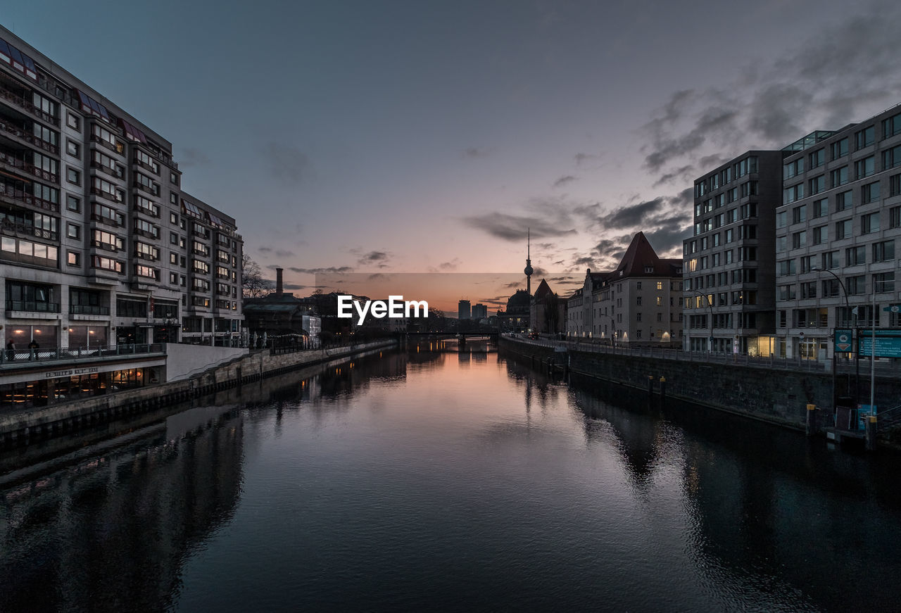 Bridge over river amidst buildings in city against sky