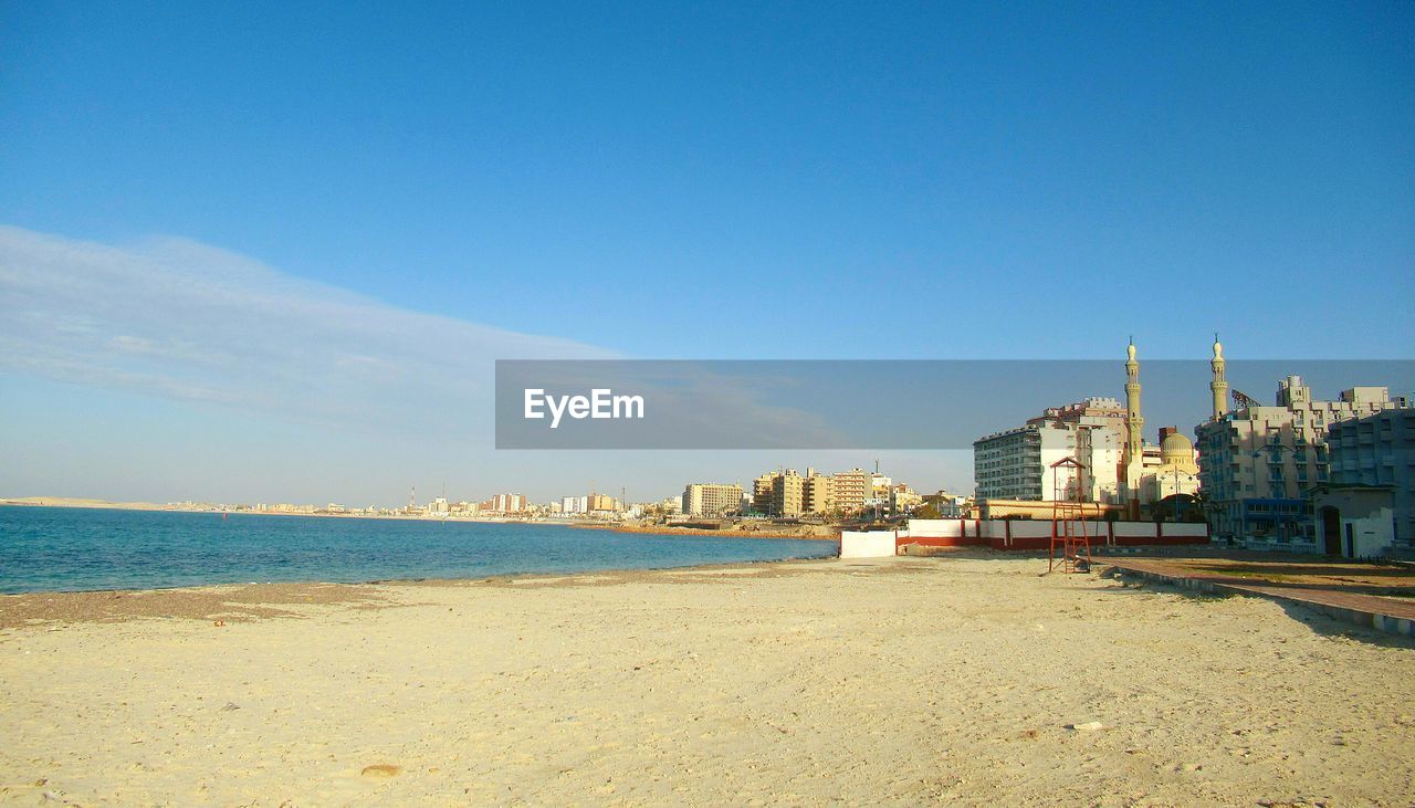 View of beach and buildings against blue sky