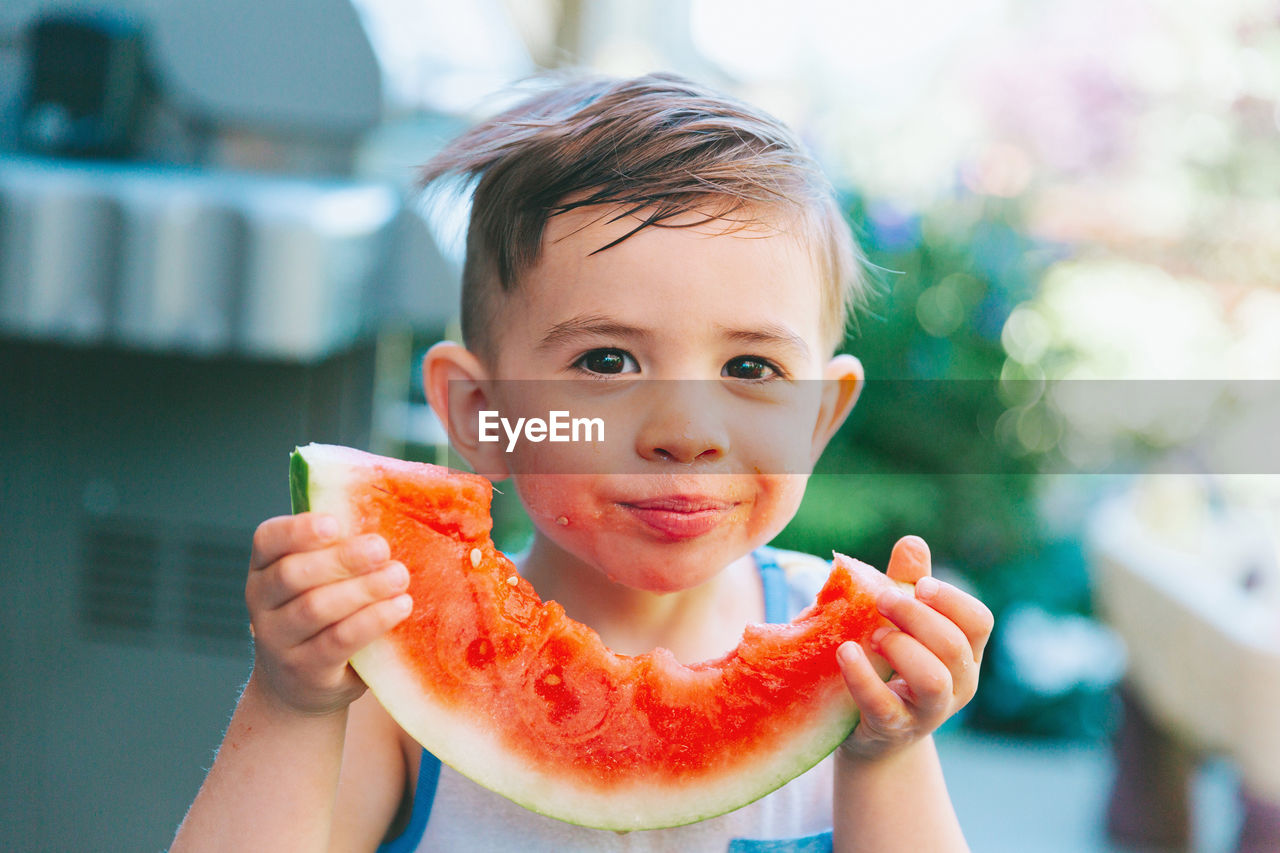 Close-up portrait of smiling boy eating watermelon while standing outdoors