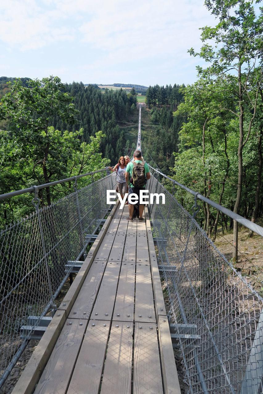 REAR VIEW OF WOMAN STANDING ON FOOTBRIDGE