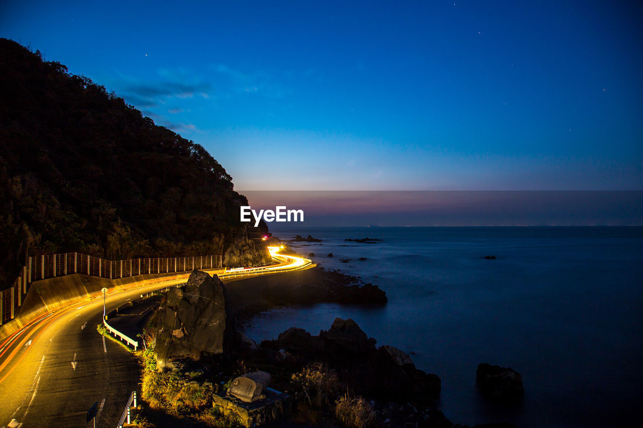 SCENIC VIEW OF ILLUMINATED SEA AGAINST SKY AT SUNSET