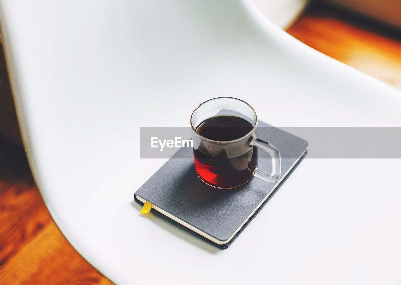 High angle view of black coffee cup and diary on white chair