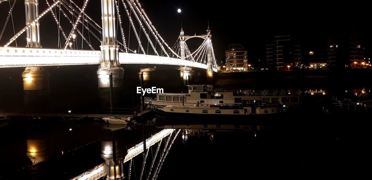 ILLUMINATED SUSPENSION BRIDGE OVER RIVER AT NIGHT