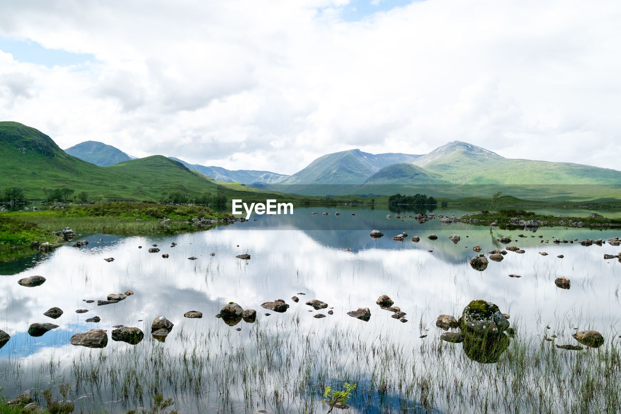 Scenic view of lake by mountains against cloudy sky