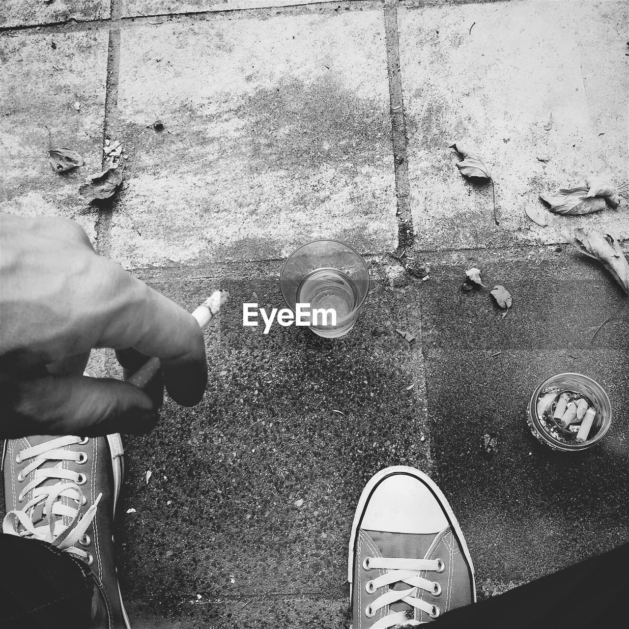 Low section of man holding cigarette by drink on sidewalk