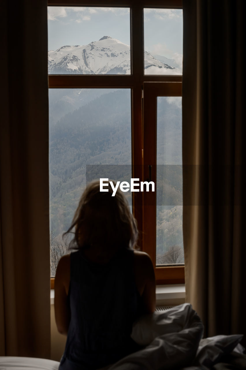 Rear view of woman looking through window at home