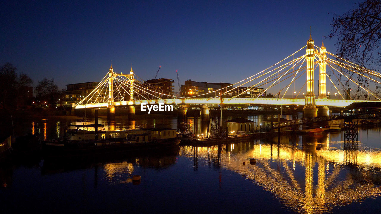 ILLUMINATED BRIDGE OVER WATER AGAINST CLEAR SKY AT DUSK