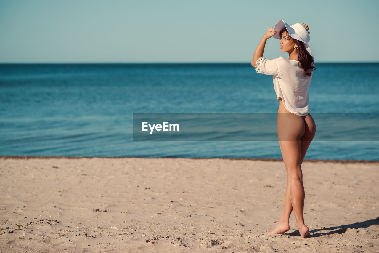 Rear view of seductive woman standing at beach during sunny day