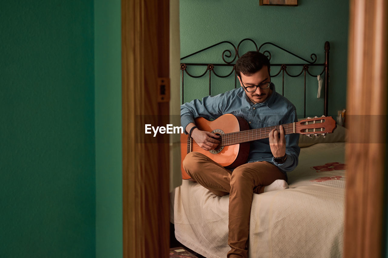 Young man plays guitar in a room in his house