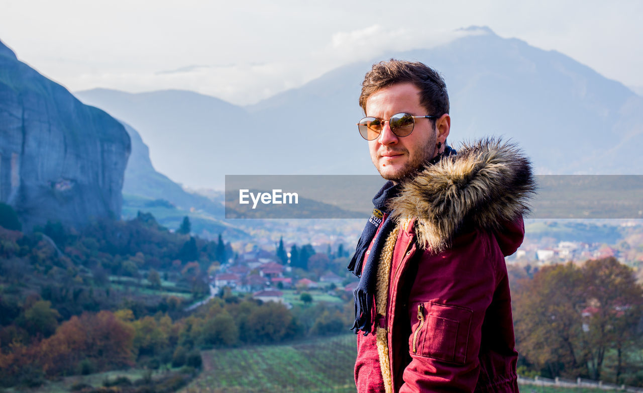 Portrait of young man wearing sunglasses standing on mountain against sky