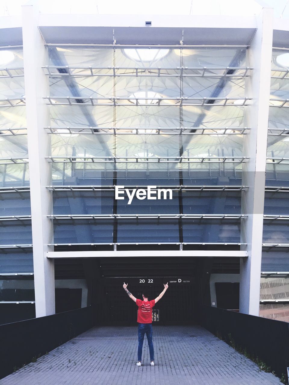 Rear view of man standing on walkway against glass building