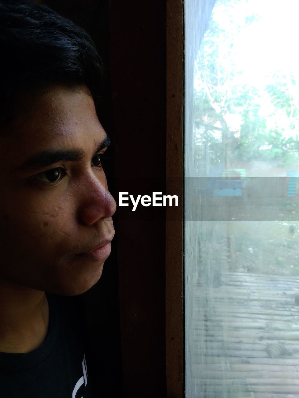 Young man looking through window at home