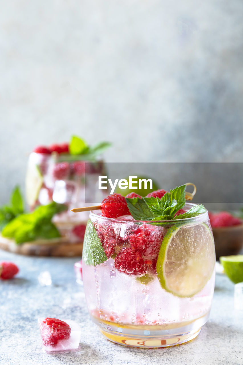 Hard seltzer cocktail with raspberries and lime on a gray stone table top. copy space.