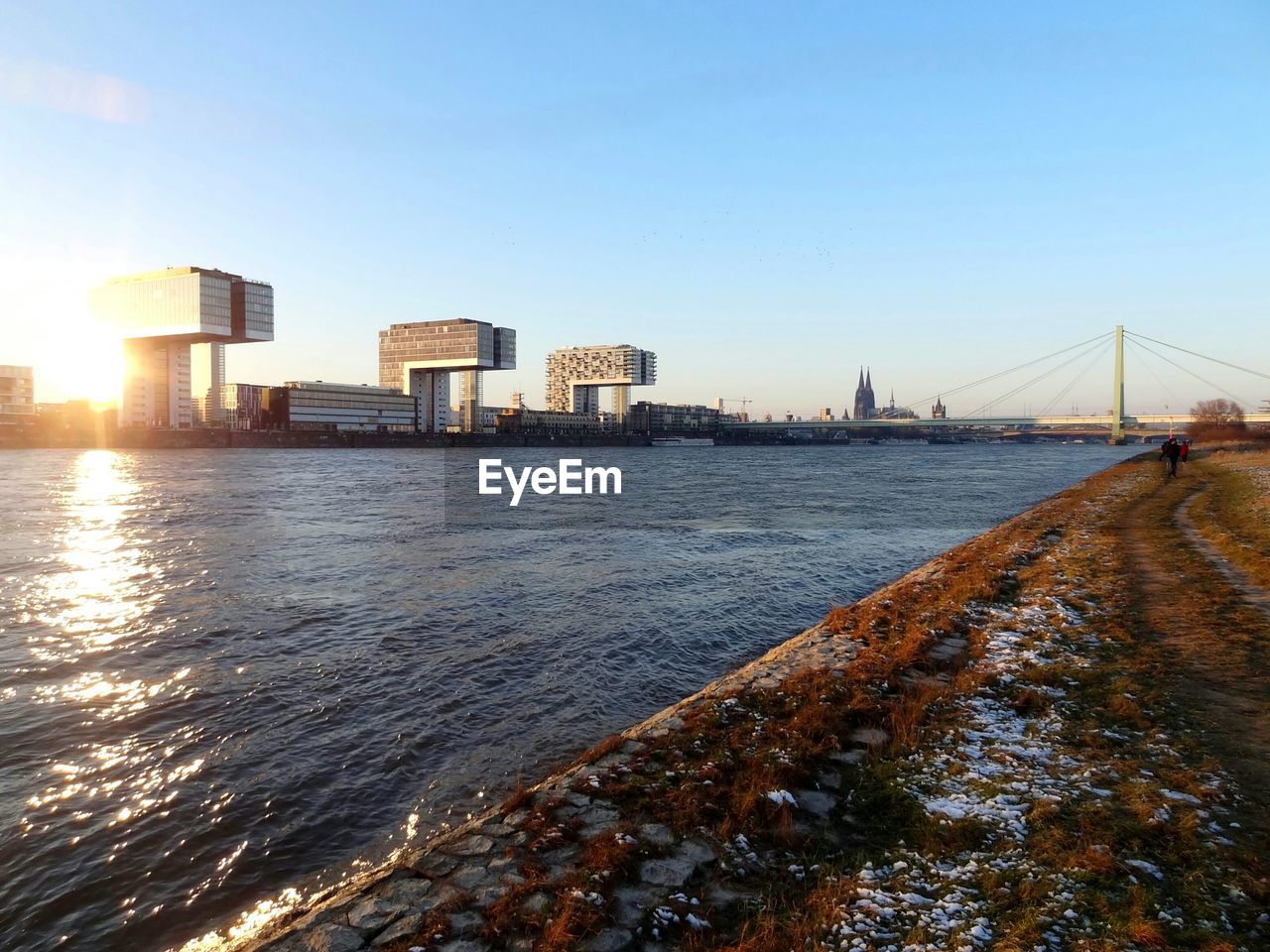 Modern buildings by river against clear blue sky