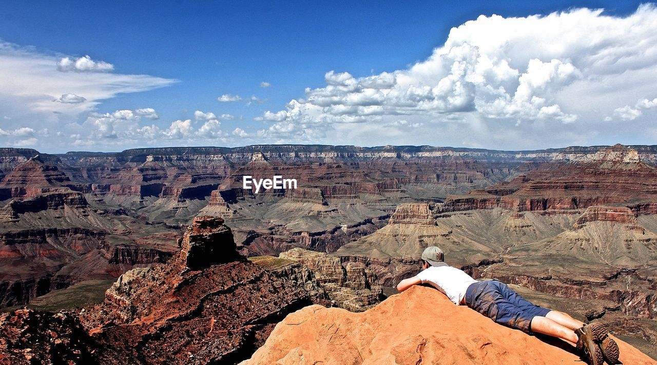 Man lying on rock formation at grand canyon against sky