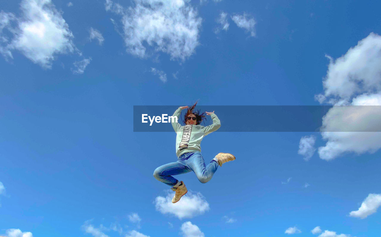Low angle view of woman jumping against blue sky