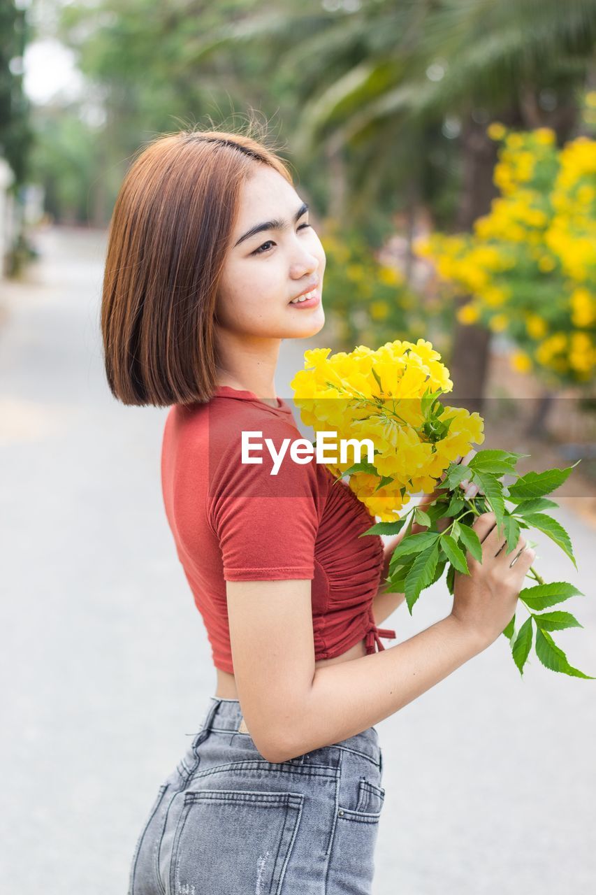 Young woman holding yellow while standing by flower