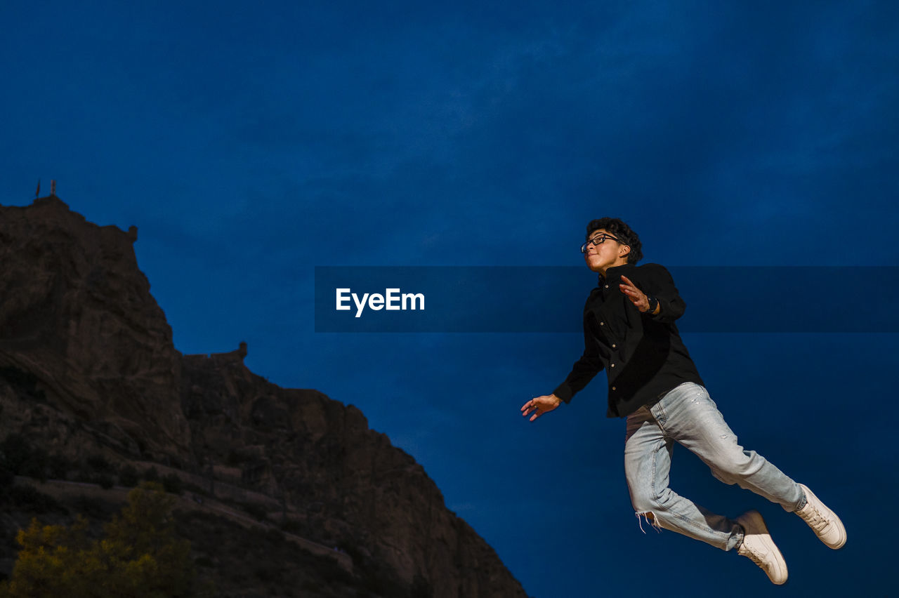 Young transgender man jumping outdoors at night.