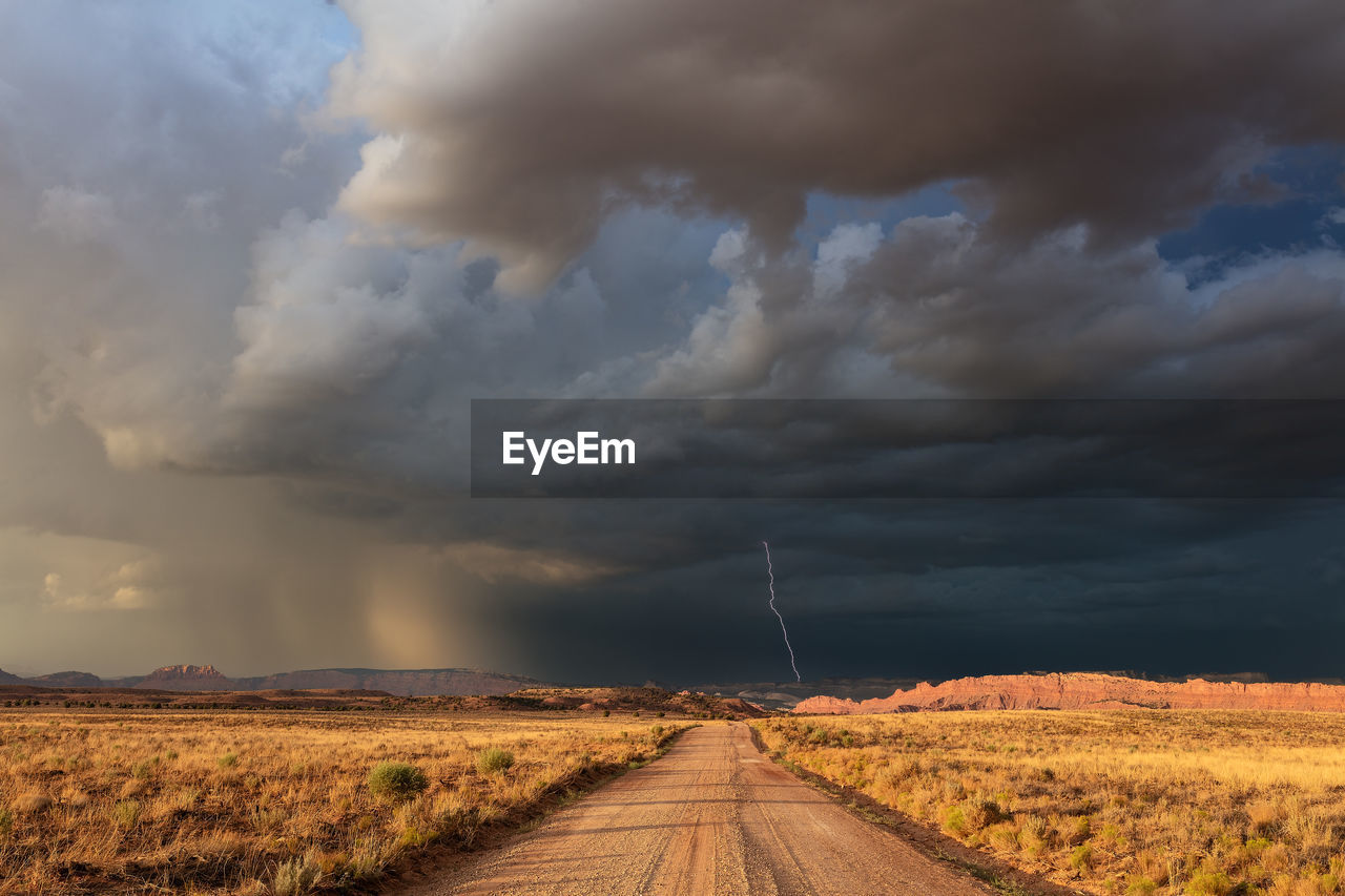 A dirt road leading to dark, ominous storm clouds and lightning in southern utah