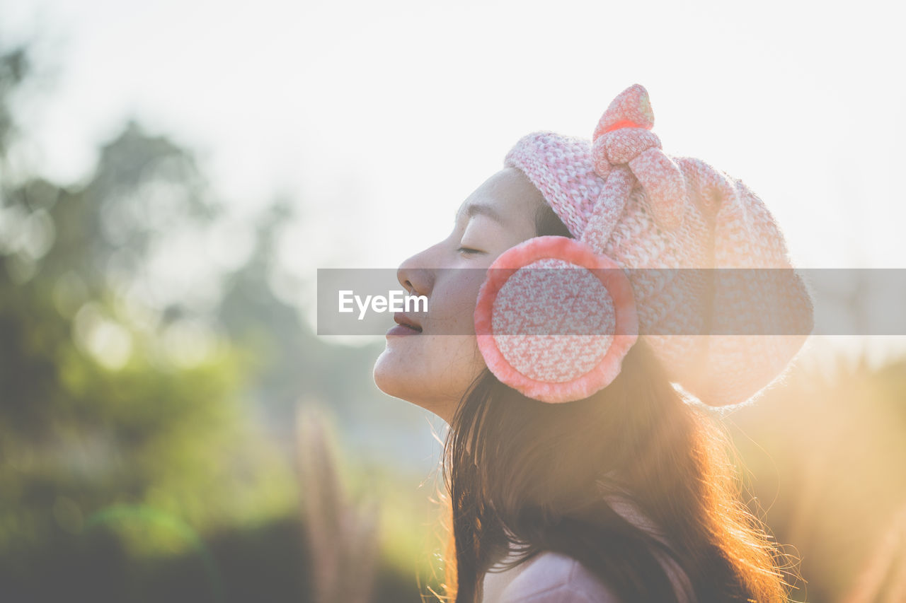 Side view of woman wearing hat and ear muffs during sunny day