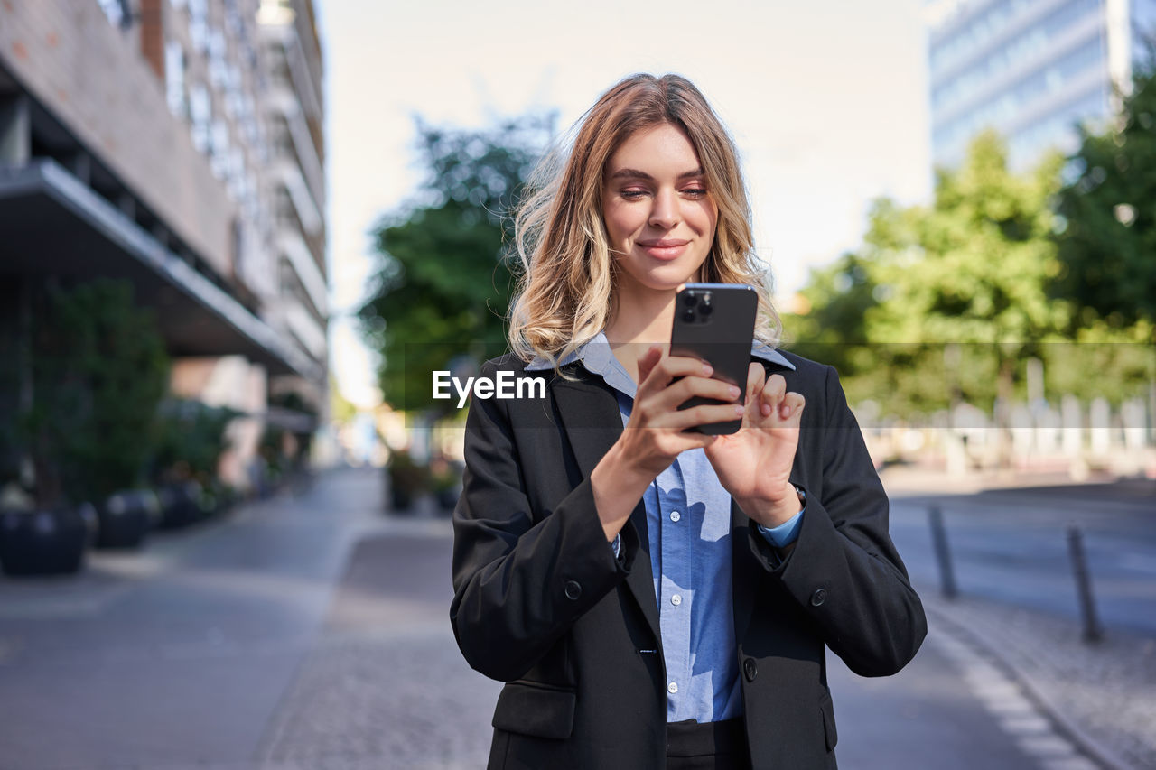 young woman using mobile phone while standing in city