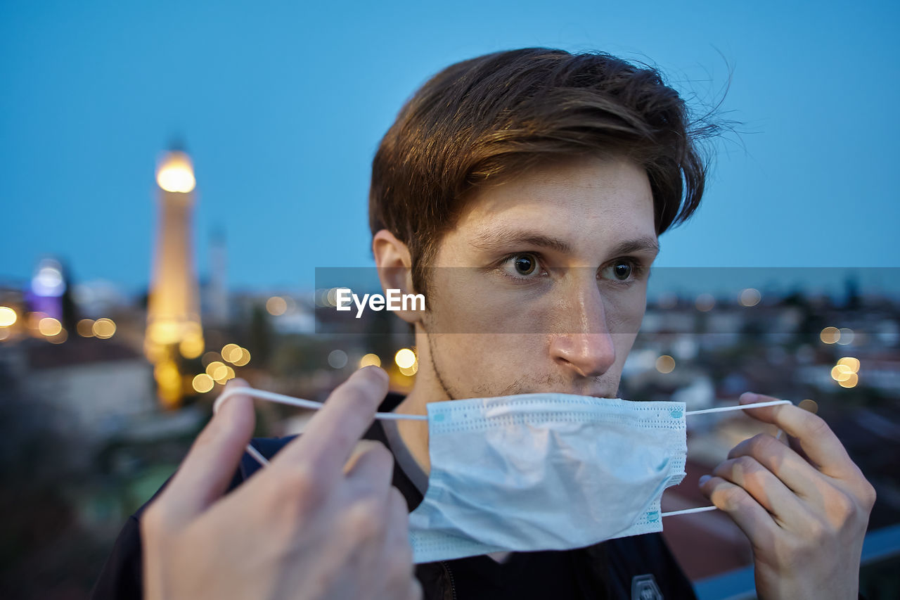 Portrait of young man holding illuminated cityscape against sky