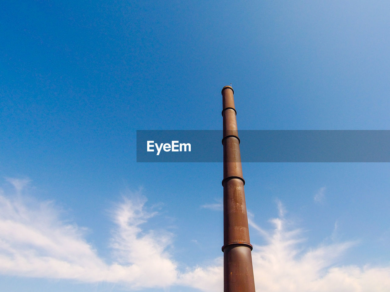 Tall industrial chimney taken from the ground on a sunny day with blue sky and beautiful clouds