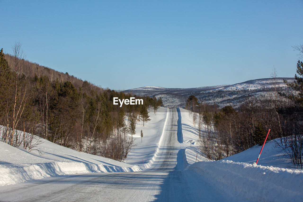 SNOW COVERED ROAD BY TREES AGAINST CLEAR SKY