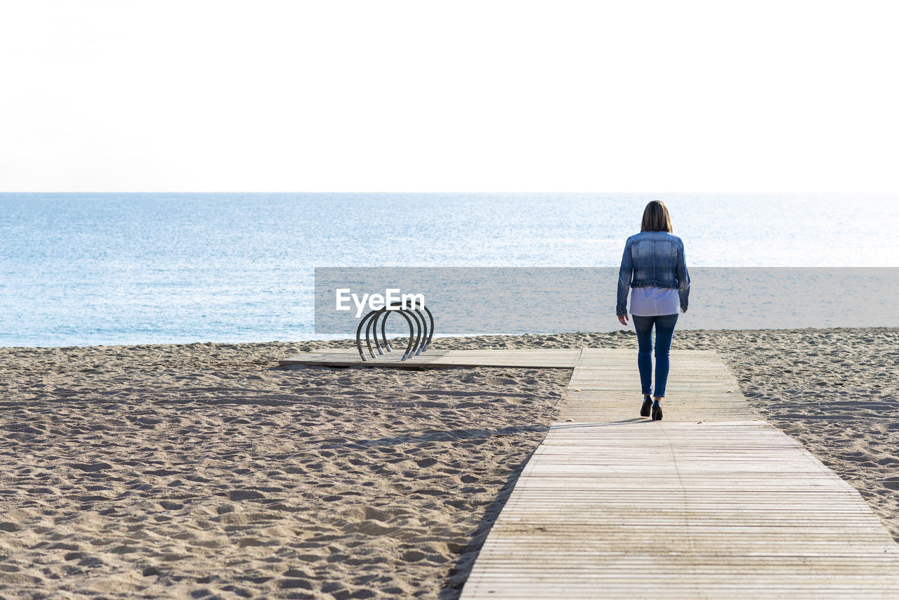 Rear view of a woman walking on footpath to seashore in sunny day