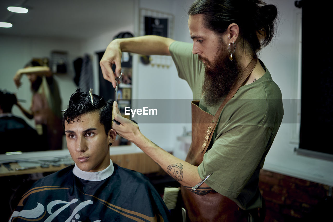 A bearded man cutting the hair of a modern young man