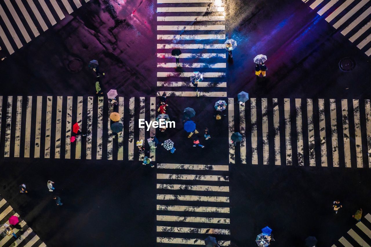 High angle view of people with umbrellas walking on road in city at night