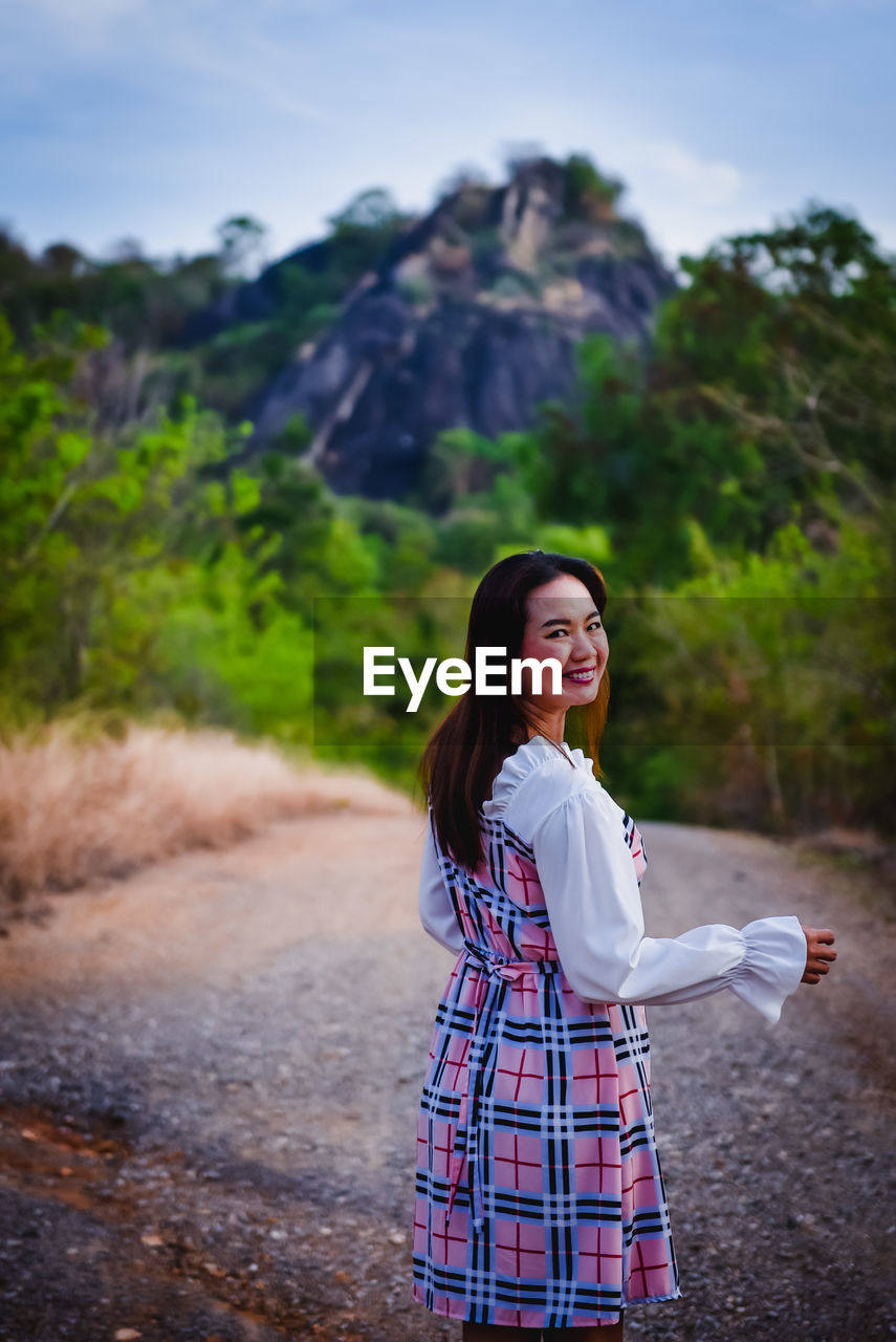 YOUNG WOMAN STANDING ON ROAD AGAINST MOUNTAIN