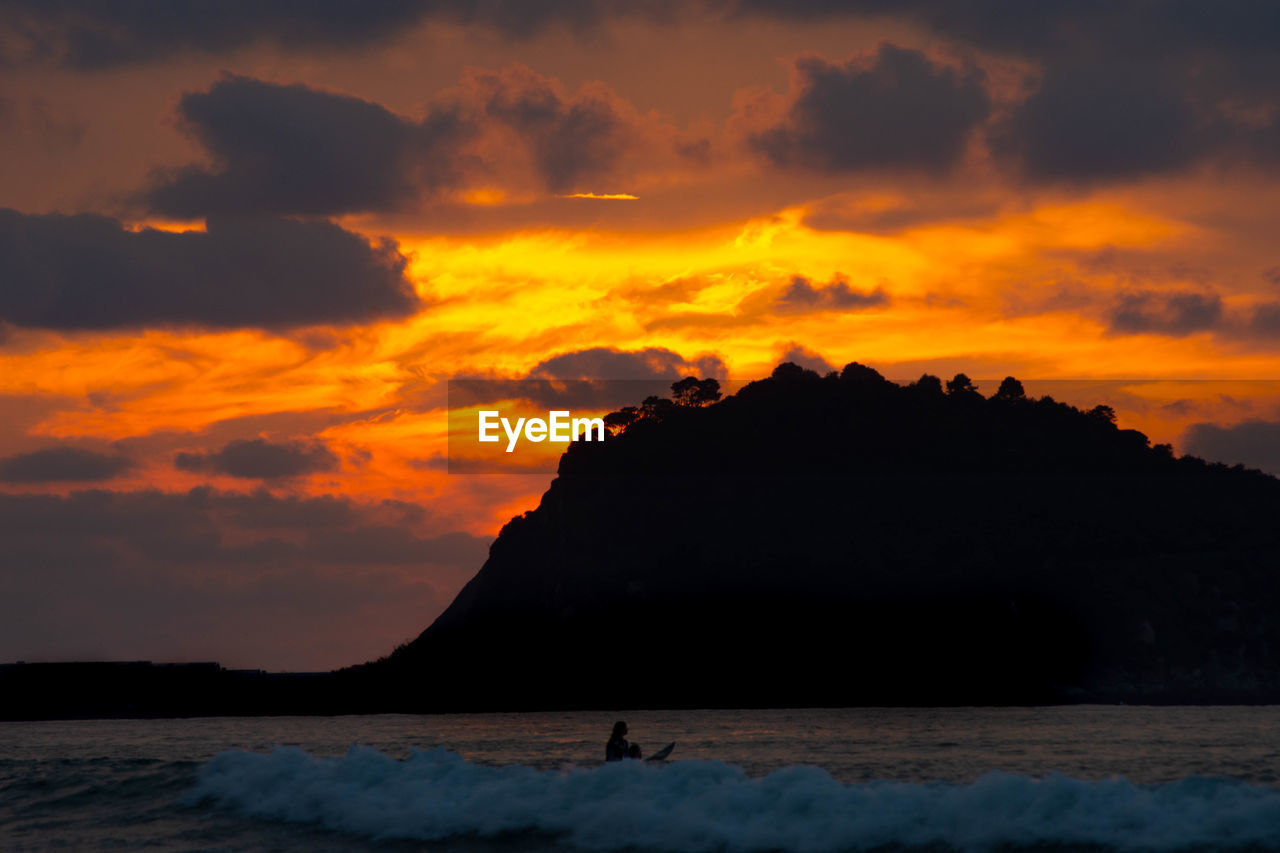 SCENIC VIEW OF SILHOUETTE MOUNTAIN AGAINST ORANGE SKY