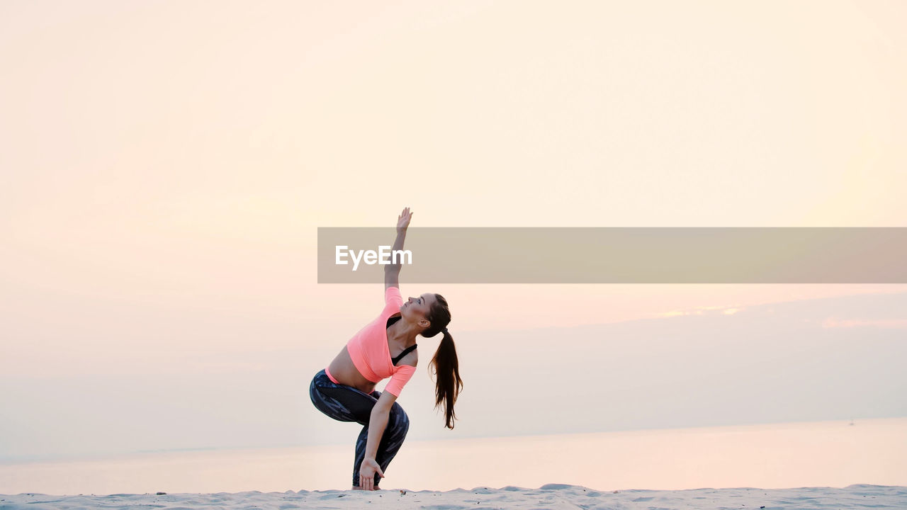 Healthy, young beautiful woman meditating, practicing yoga on the sea beach, at sunrise, makes