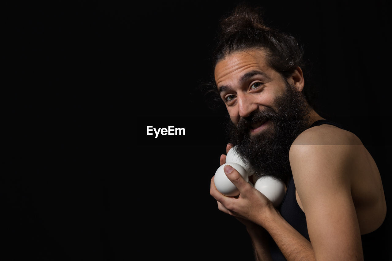 Portrait of bearded man with balls while standing against black background