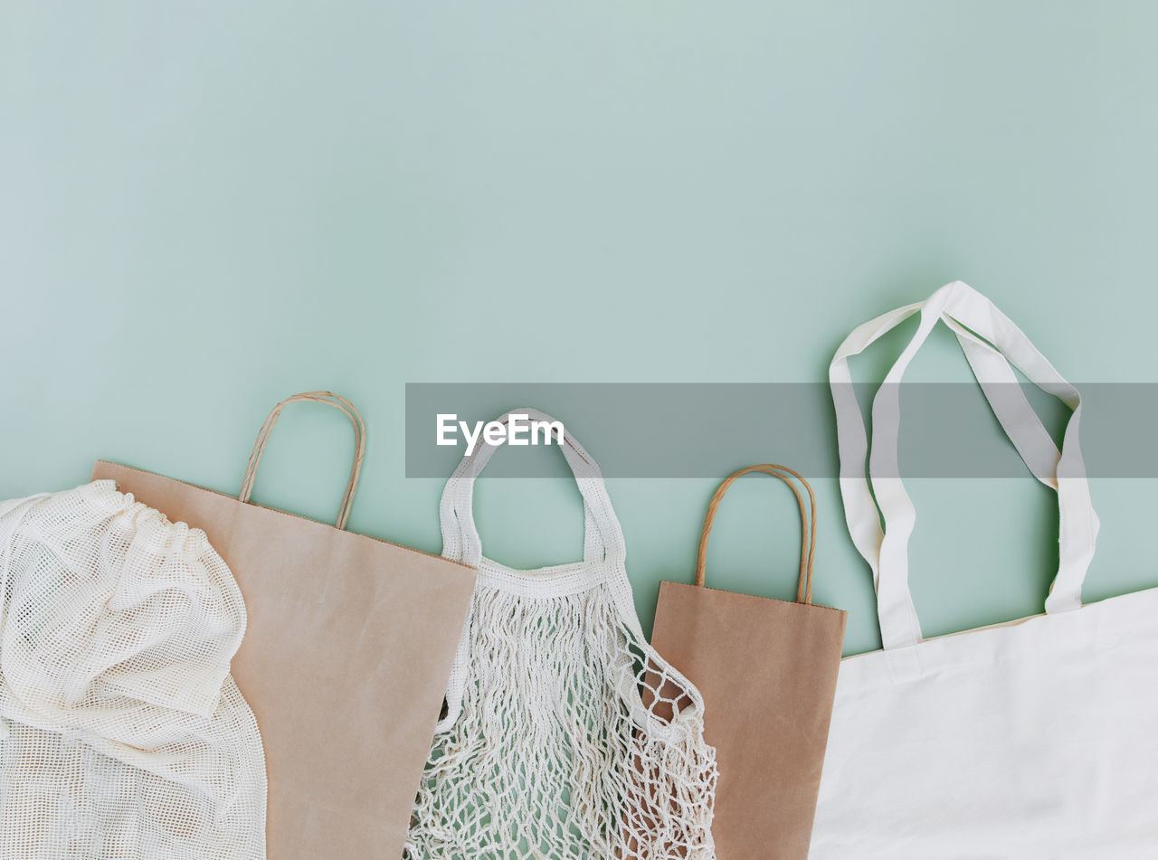 Flat lay with eco white craft paper bags and net bags on green background with empty copy space