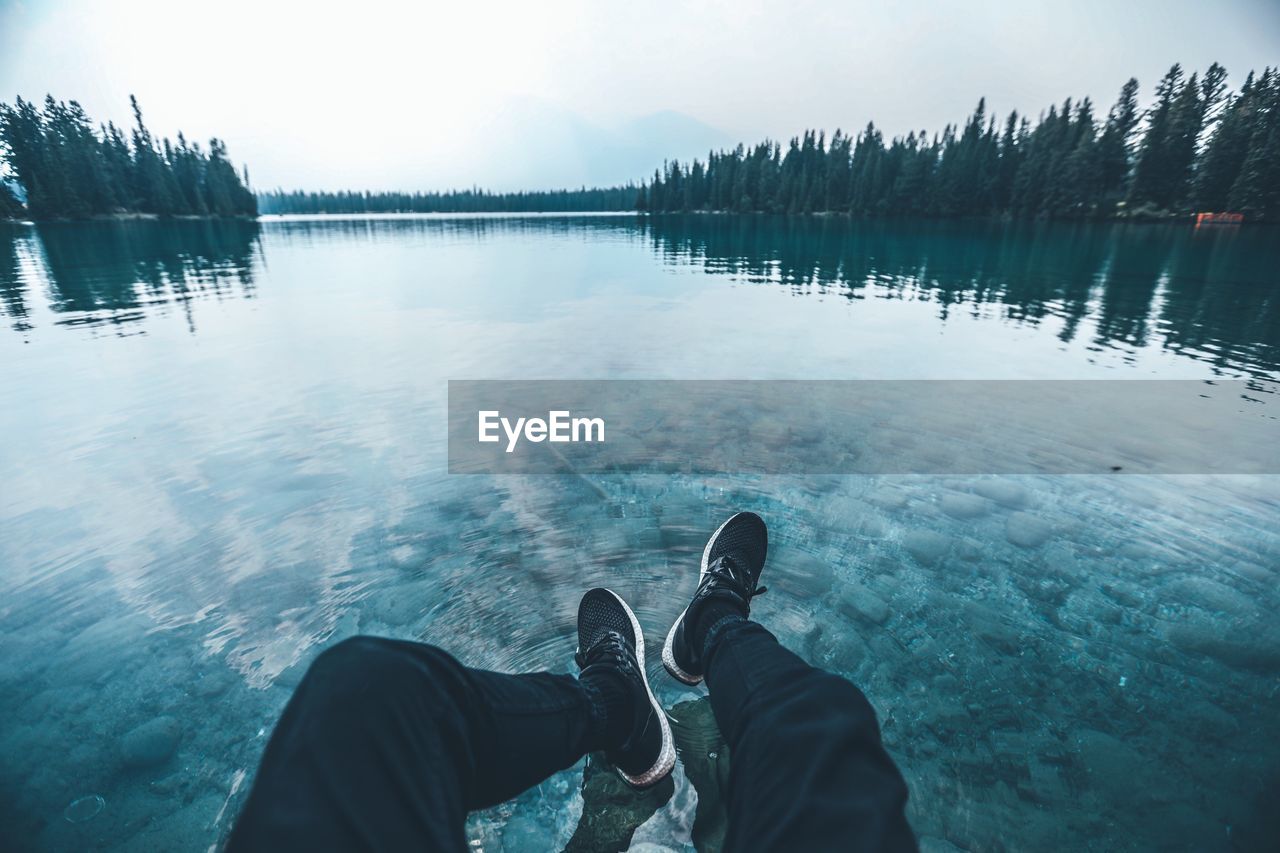 Low section of man sitting by lake against sky