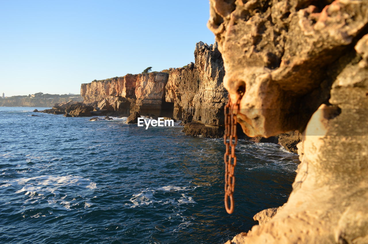 Rock formations by sea against clear sky