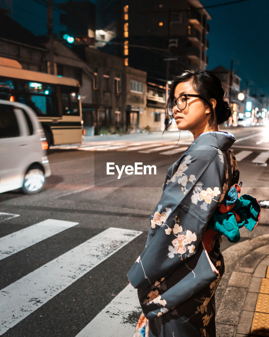 Side view of young woman in traditional clothing waiting at zebra crossing in city