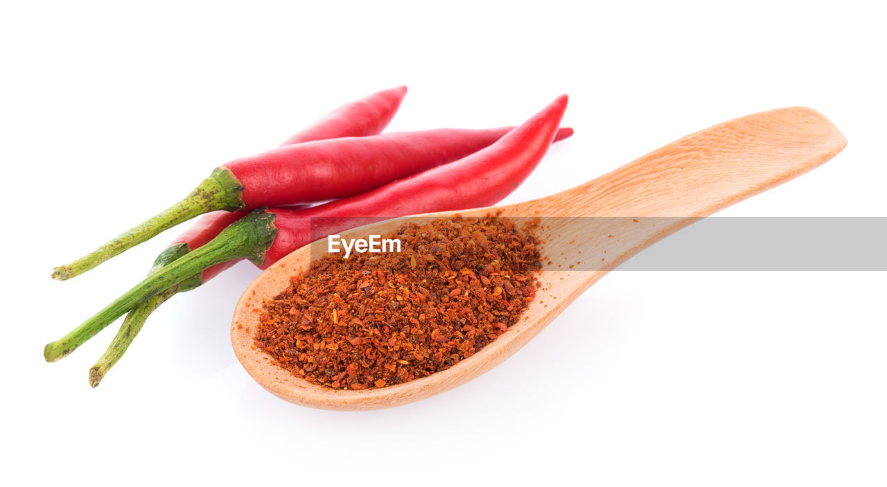 Close-up of red chili peppers and spoon on white background