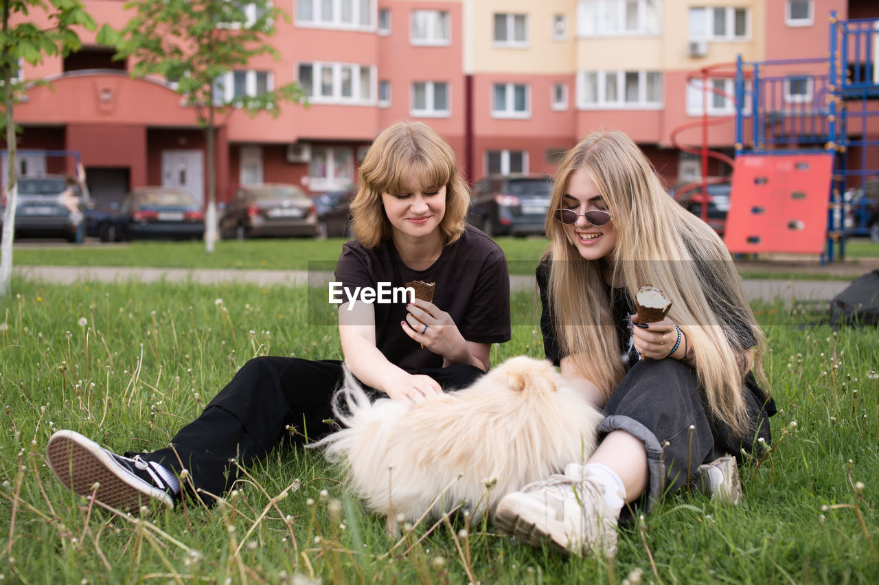 Two funny girls are eating ice cream and playing with a pomeranian dog. holidays