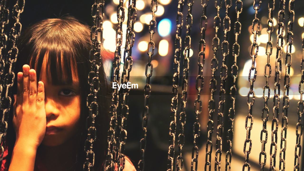 Close-up portrait of cute girl standing by chains