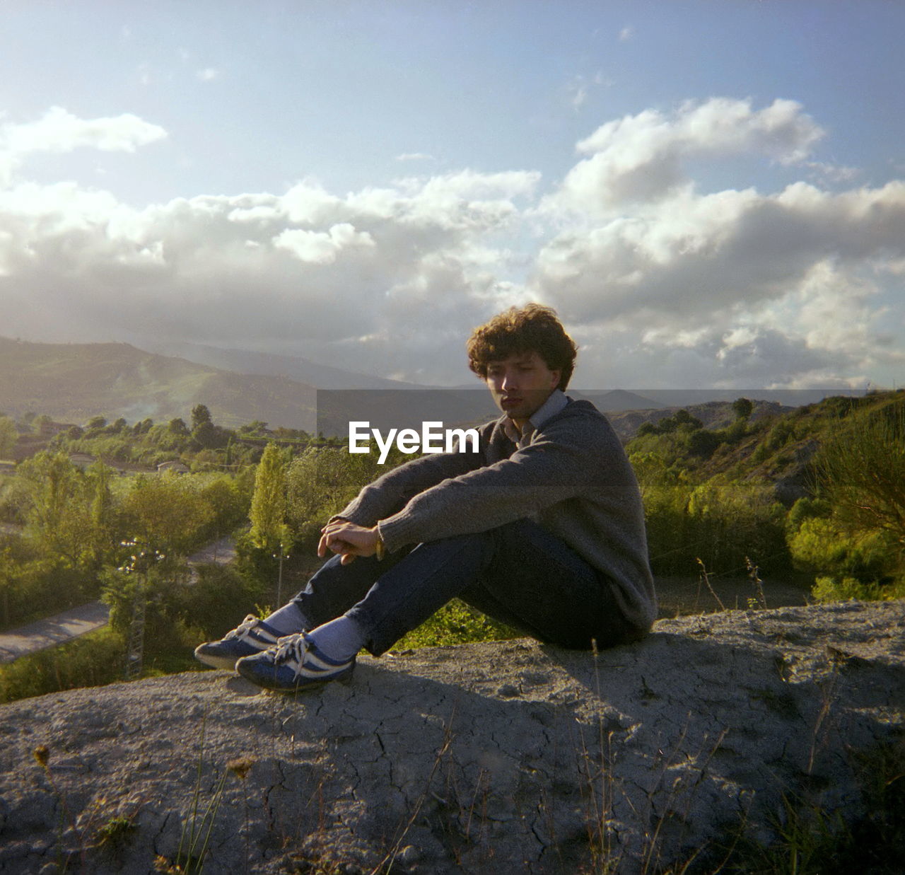 Side view of young man sitting on mountain against sky