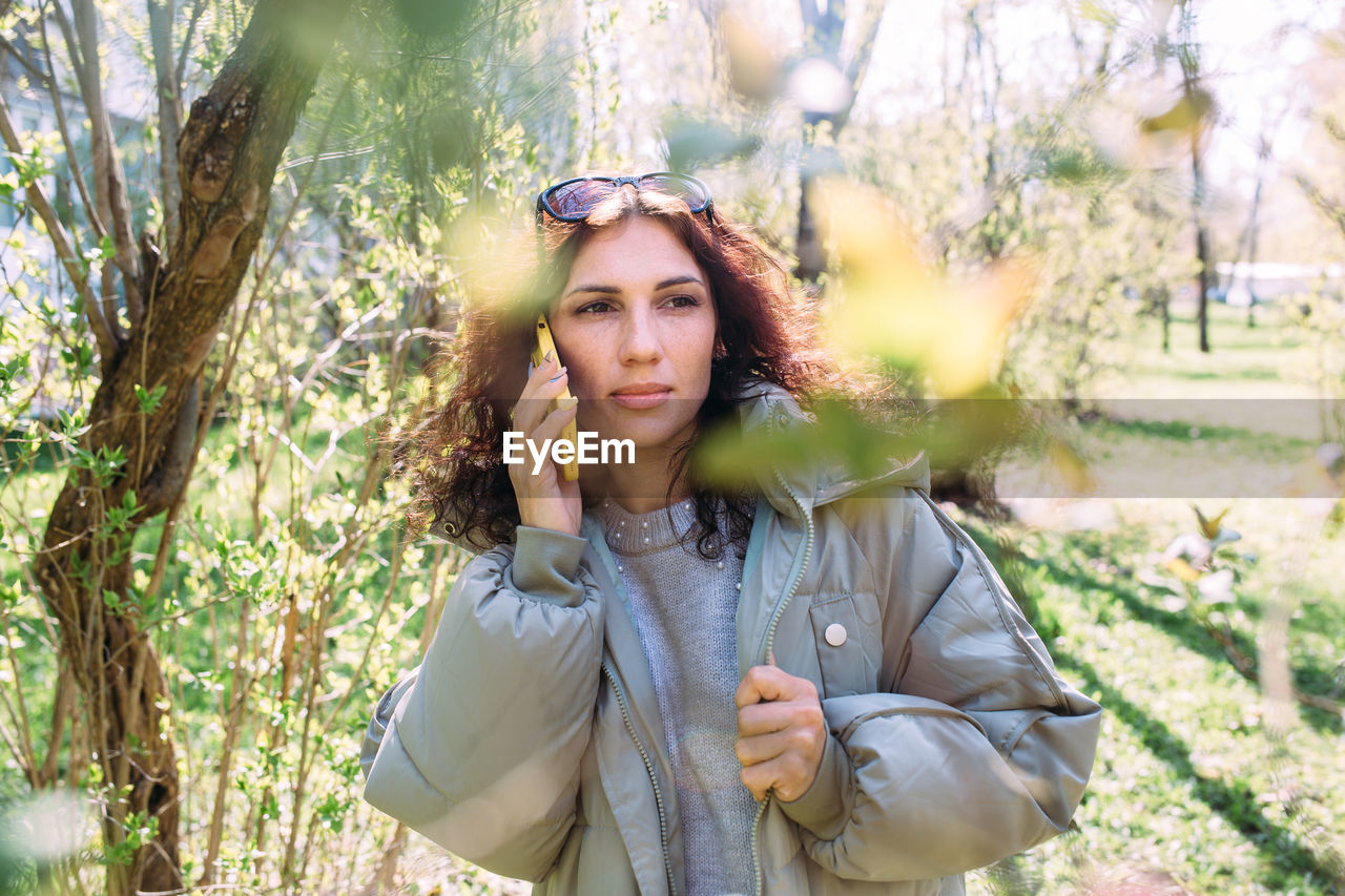 Young brunette woman talking on the phone in spring in the park