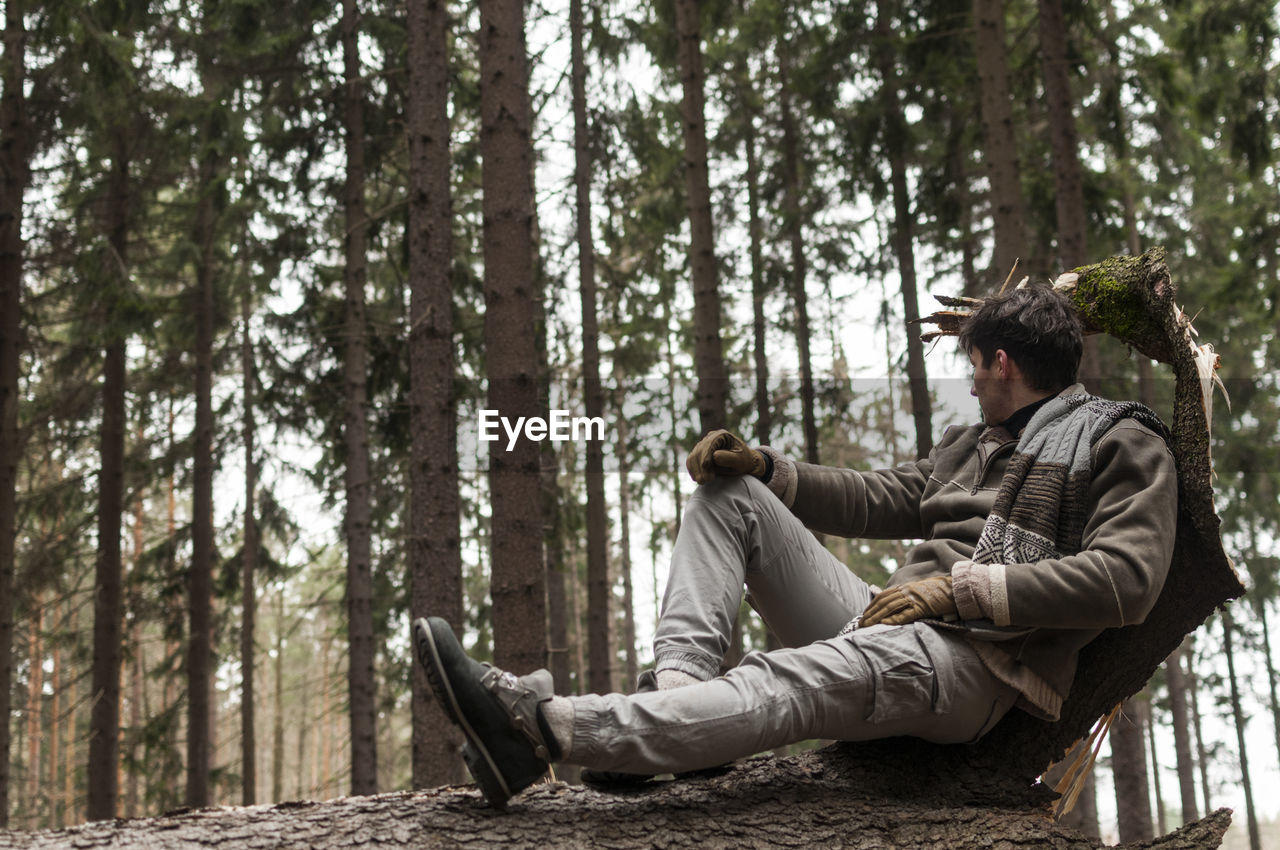 Young man sitting on log in forest