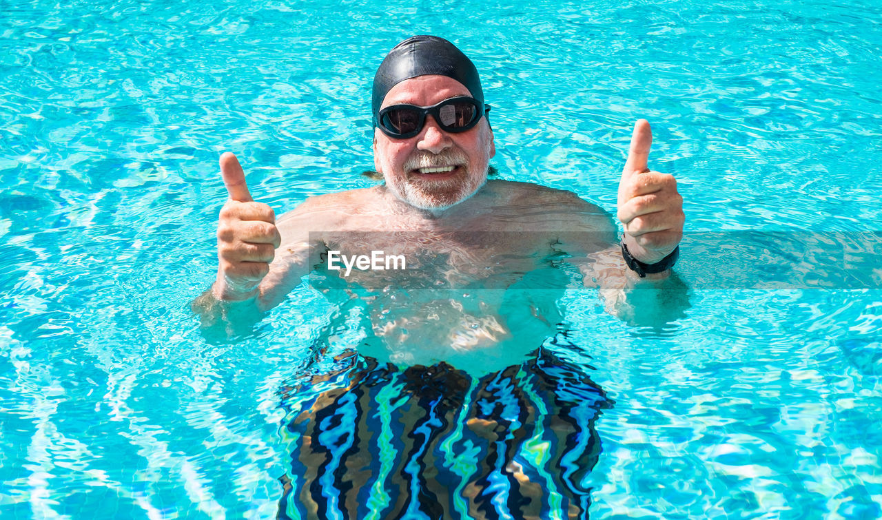 PORTRAIT OF SMILING YOUNG MAN SWIMMING IN POOL