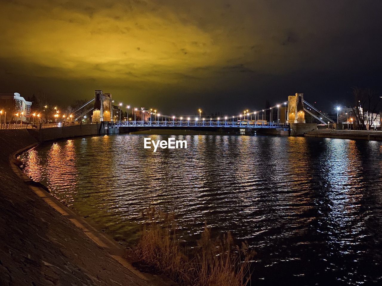 ILLUMINATED BRIDGE OVER RIVER AGAINST SKY IN CITY